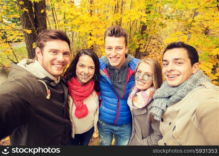 technology, season, friendship and people concept - group of smiling men and women taking selfie with smartphone or camera in autumn park