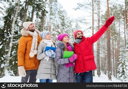 technology, season, friendship and people concept - group of smiling men and women with tablet pc computers pointing finger in winter forest