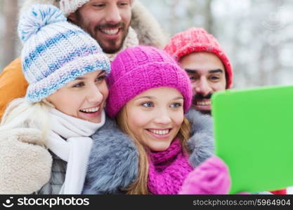 technology, season, friendship and people concept - group of smiling men and women taking selfie tablet pc computer in winter forest