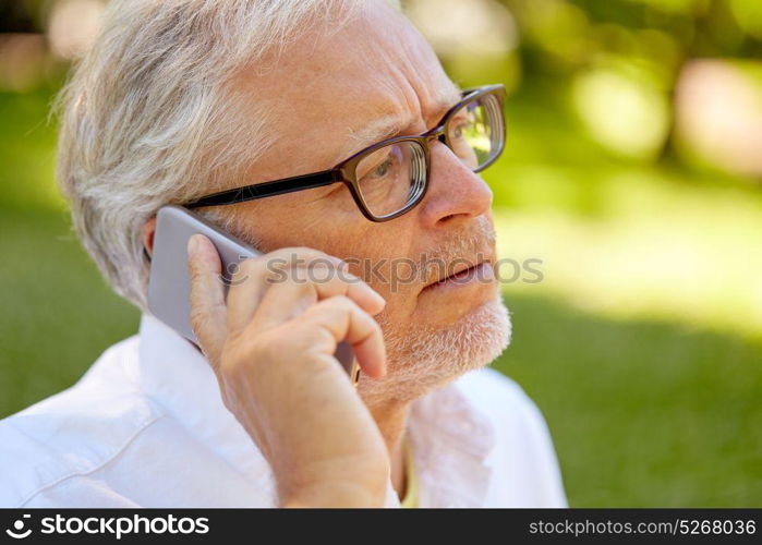 technology, senior people, and communication concept - close up of old man in glasses calling on smartphone at summer park. senior man in glasses calling on smartphone