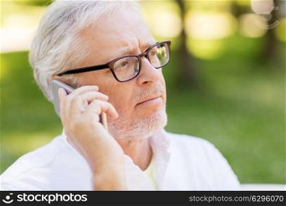 technology, senior people, and communication concept - close up of sad old man in glasses calling on smartphone at summer park. sad senior man in glasses calling on smartphone