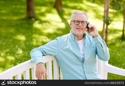 technology, senior people, and communication concept - happy old man calling on smartphone sitting on bench at summer park