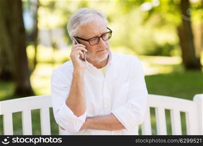 technology, senior people, and communication concept - old man in glasses calling on smartphone at summer park. senior man calling on smartphone at summer park