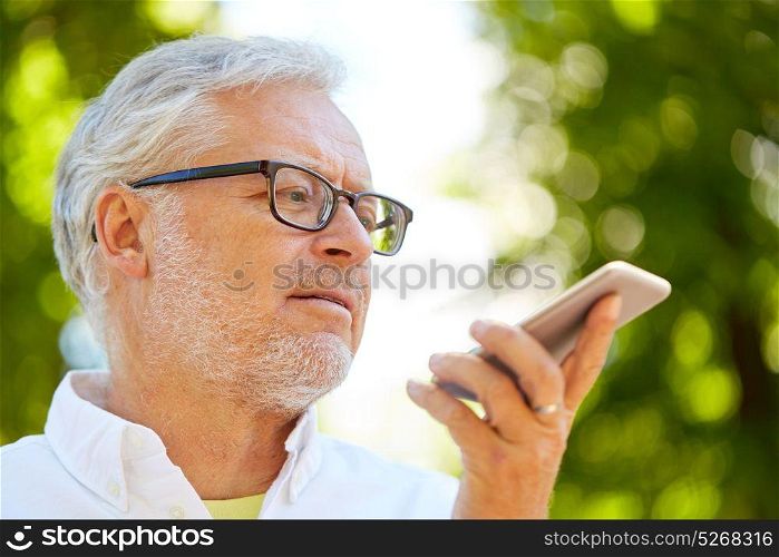 technology, senior people and communication concept - old man using voice command recorder or calling on smartphone at summer park. old man using voice command recorder on smartphone