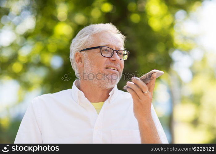 technology, senior people and communication concept - old man using voice command recorder or calling on smartphone at summer park. old man using voice command recorder on smartphone