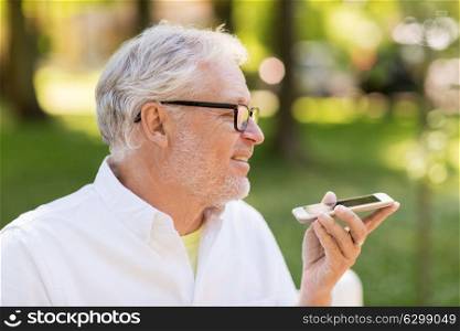 technology, senior people and communication concept - old man using voice command recorder or calling on smartphone at summer park. old man using voice command recorder on smartphone