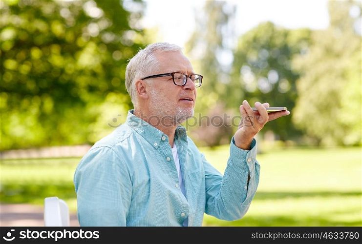 technology, senior people, lifestyle and communication concept - close up of happy old man using voice command recorder or calling on smartphone at summer park