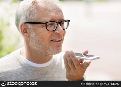 technology, senior people, lifestyle and communication concept - close up of happy old man using voice command recorder or calling on smartphone outdoors