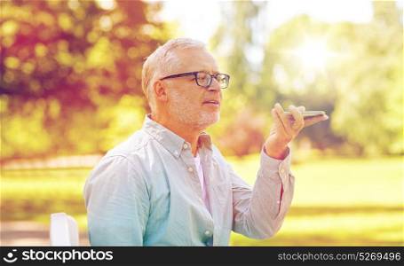 technology, senior people, lifestyle and communication concept - close up of happy old man using voice command recorder or calling on smartphone at summer park. old man using voice command recorder on smartphone