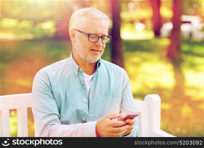 technology, senior people, lifestyle and communication concept - happy old man dialing phone number and texting on smartphone at summer park. happy senior man texting on smartphone at summer
