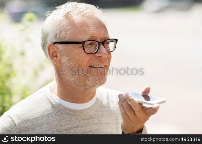 technology, senior people, lifestyle and communication concept - happy old man using voice command recorder or calling on smartphone outdoors. old man using voice command recorder on smartphone