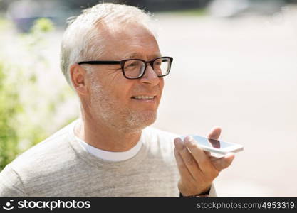 technology, senior people, lifestyle and communication concept - happy old man using voice command recorder or calling on smartphone outdoors. old man using voice command recorder on smartphone