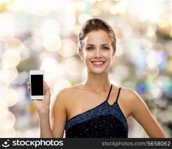 technology, smartphone, advertisement and people concept - smiling woman in evening dress holding smartphone over holidays lights background