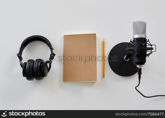 technology, sound recording and podcast concept - headphones , microphone and notebook with pencil on white background. headphones, microphone and notebook with pencil