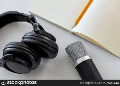 technology, sound recording and podcast concept - headphones , microphone and notebook with pencil on white background. headphones, microphone and notebook with pencil
