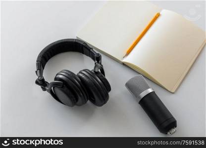 technology, sound recording and podcast concept - headphones , microphone and notebook with pencil on white background. headphones, microphone and notebook with pencil