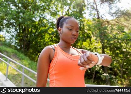 technology, sport and fitness concept - young african american woman with smart watch outdoors. african woman with smart watch doing sports