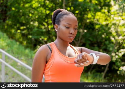 technology, sport and fitness concept - young african american woman with smart watch outdoors. african woman with smart watch doing sports