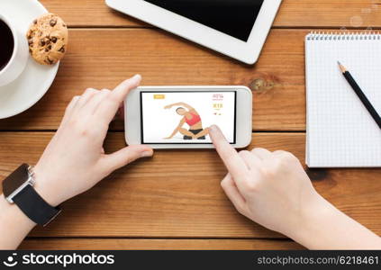 technology, sport and people concept - close up of woman with fitness application on smartphone screen and coffee cup on wooden table