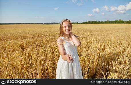 technology, summer and people concept - happy young girl in white dress taking picture by selfie stick on cereal field. happy girl taking selfie on cereal field