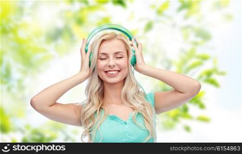 technology, summer and people concept - happy young woman or teenage girl with headphones listening to music over green natural background
