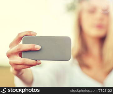 technology, summer holidays, vacation and people concept - close up of young woman in wreath of flowers taking picture by smartphone on cereal field. close up of woman taking selfie by smartphone