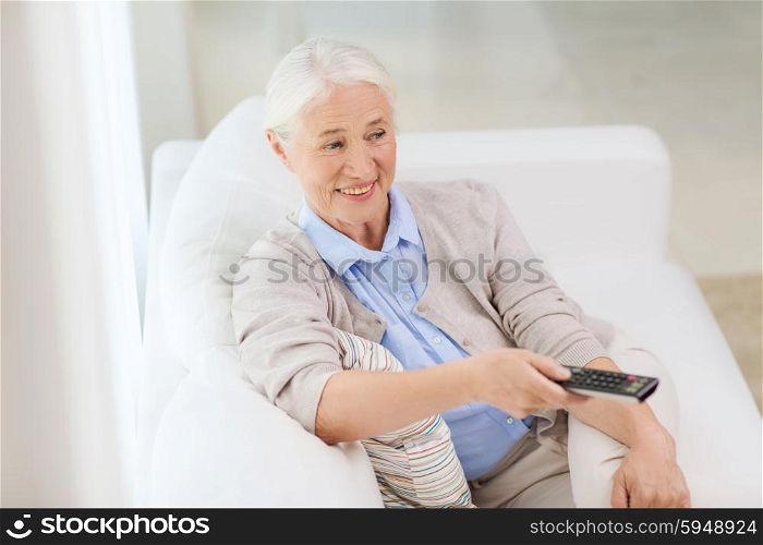 technology, television, age and people concept - happy senior woman watching tv and changing channel with remote control at home