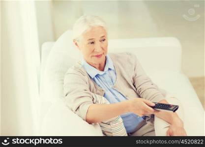 technology, television, age and people concept - senior woman watching tv and changing channel with remote control at home