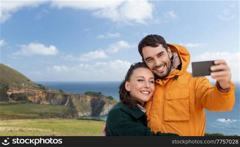 technology, travel and tourism concept - happy couple with smartphone over big sur coast in california background. couple with smartphone over coast in california