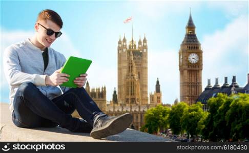 technology, travel, tourism and people concept - smiling young man or teenage boy with tablet pc computers over london city and big ben tower background
