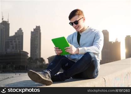technology, travel, tourism and people concept - smiling young man or teenage boy with tablet pc computers over dubai city street background