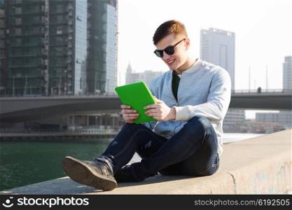 technology, travel, tourism and people concept - smiling young man or teenage boy with tablet pc computers over dubai city street background