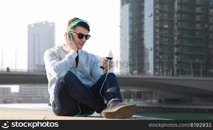 technology, travel, tourism and people concept - smiling young man or teenage boy in headphones with smartphone listening to music over dubai city street background