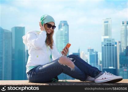 technology, travel, tourism and people concept - smiling young woman or teenage girl with smartphone and headphones listening to music over singapore city background