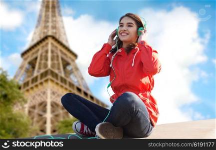 technology, travel, tourism and people concept - smiling young woman or teenage girl in headphones listening to music over paris eiffel tower background