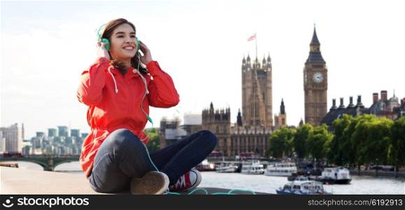 technology, travel, tourism and people concept - smiling young woman or teenage girl in headphones listening to music over london city and big ben tower background