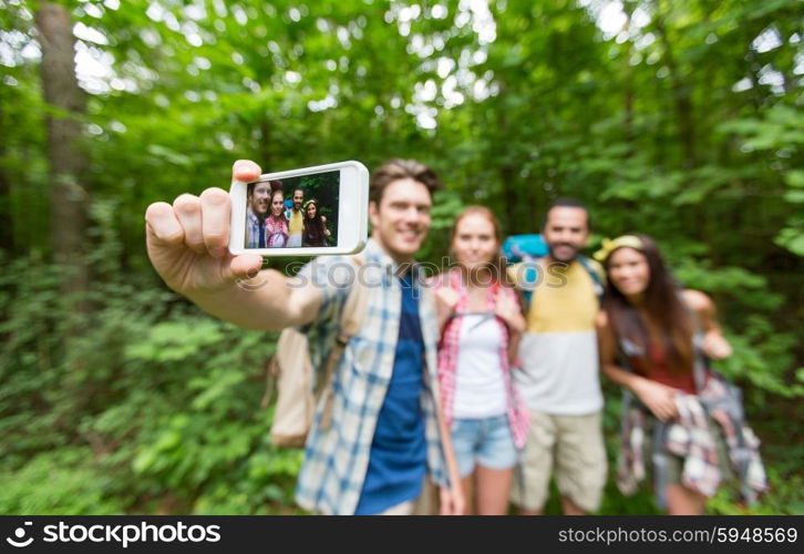 technology, travel, tourism, hike and people concept - close up of happy friends walking with backpacks taking selfie by smartphone in woods