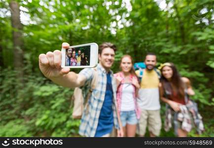 technology, travel, tourism, hike and people concept - close up of happy friends walking with backpacks taking selfie by smartphone in woods
