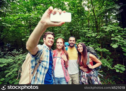 technology, travel, tourism, hike and people concept - group of smiling friends walking with backpacks taking selfie by smartphone in woods