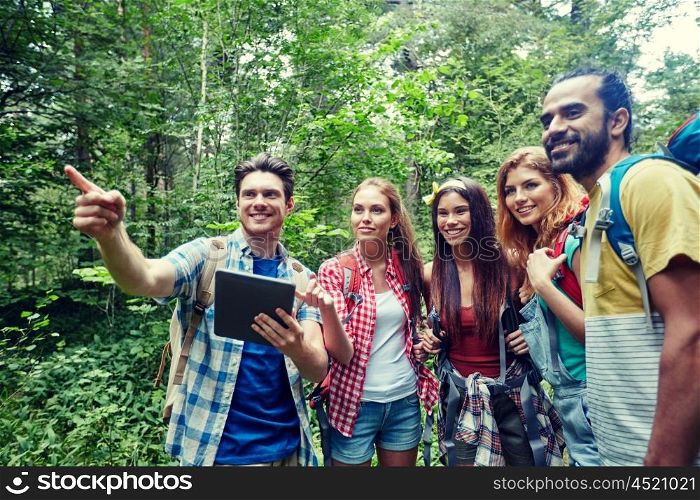 technology, travel, tourism, hike and people concept - group of smiling friends walking with backpacks and tablet pc computer looking for location in woods