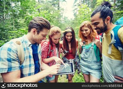 technology, travel, tourism, hike and people concept - group of smiling friends walking with backpacks and map on tablet pc computer screen looking for location in woods