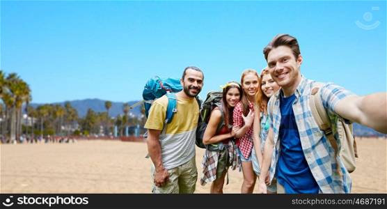 technology, travel, tourism, hike and people concept - group of smiling friends with backpacks taking selfie over big sur coast of california background. friends with backpacks taking selfie. friends with backpacks taking selfie