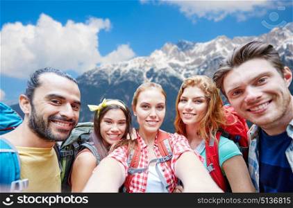 technology, travel, tourism, hike and people concept - group of smiling friends with backpacks taking selfie over alps mountains background. friends with backpack taking selfie over mountains. friends with backpack taking selfie over mountains