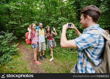 technology, travel, tourism, hike and people concept - group of smiling friends with backpacks taking picture by smartphone and waving hands in woods