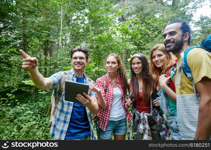 technology, travel, tourism, hike and people concept - group of smiling friends walking with backpacks and tablet pc computer looking for location in woods