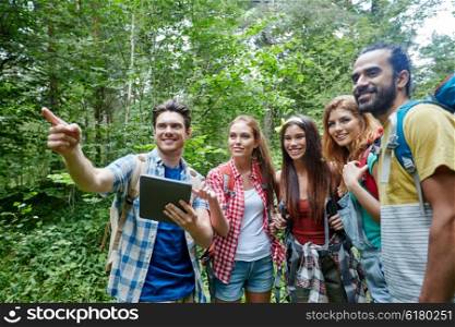 technology, travel, tourism, hike and people concept - group of smiling friends walking with backpacks and tablet pc computer looking for location in woods