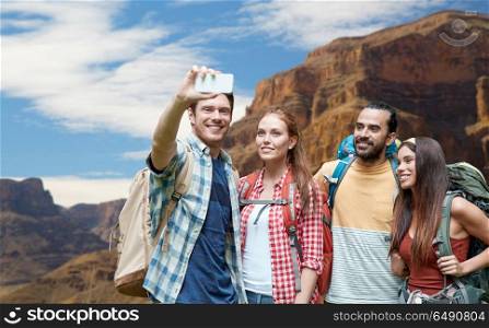 technology, travel, tourism, hike and people concept - group of smiling friends with backpacks taking selfie by smartphone over grand canyon national park background. friends with backpack taking selfie by smartphone. friends with backpack taking selfie by smartphone