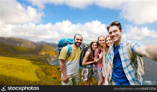 technology, travel, tourism, hike and people concept - group of smiling friends with backpacks taking selfie over big sur coast of california background. friends with backpacks taking selfie. friends with backpacks taking selfie