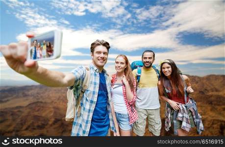technology, travel, tourism, hike and people concept - group of smiling friends with backpacks taking selfie by smartphone over grand canyon national park hills background. friends with backpack taking selfie by smartphone. friends with backpack taking selfie by smartphone