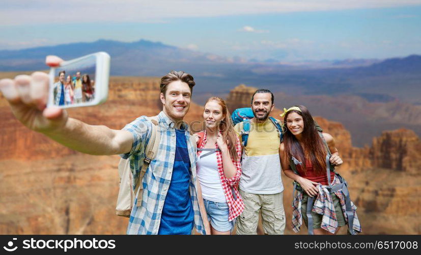 technology, travel, tourism, hike and people concept - group of smiling friends with backpacks taking selfie by smartphone over grand canyon national park background. friends with backpack taking selfie by smartphone. friends with backpack taking selfie by smartphone